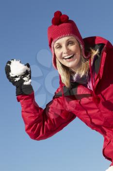Woman About To Throw Snowball Wearing Warm Clothes On Ski Holiday In Mountains