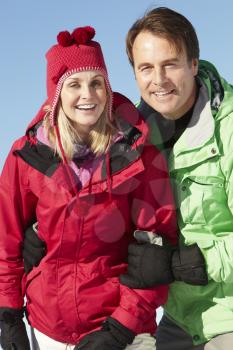 Couple Standing In Snow Wearing Warm Clothes On Ski Holiday In Mountains