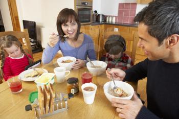 Family Eating Breakfast Together In Kitchen Whilst Children Play With Gadgets