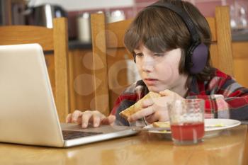 Boy Using Laptop Whilst Eating Breakfast