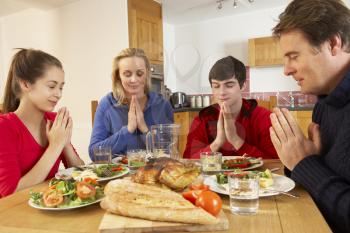 Teenage Family Saying Grace Before Eating Lunch Together In Kitchen