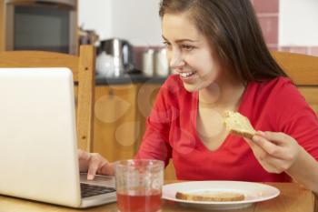 Teenage Girl Using Laptop Whilst Eating Breakfast
