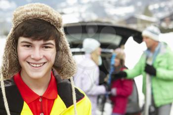 Teenage Boy Smiling At Camera Whilst Family Load Skis In Boot Of Car