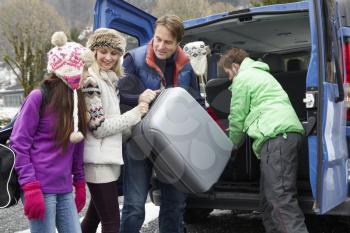 Family Unloading Luggage From Transfer Van Outside Chalet On Ski Holiday