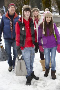 Teenage Family Carrying Shopping Walking Along Snowy Street