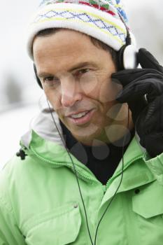 Man Wearing Headphones And Listening To Music Wearing Winter Clothes In Snowy Landscape
