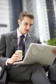 Businessman Working On Laptop Outside Office With Takeaway Coffee