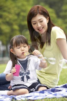 Chinese Mother With Daughter In Park Blowing Bubbles