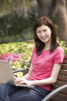 Young Chinese Woman Using Laptop Whilst  Relaxing On Park Bench