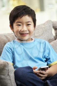 Young Chinese Boy Using Mobile Phone On Sofa At Home