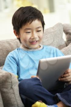 Young Chinese Boy Using Tablet Computer Whilst Sitting On Sofa At Home