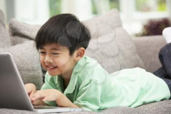 Young Chinese Boy Using Laptop Whilst Relaxing On Sofa At Home