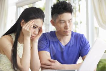 Worried Young Chinese Couple Sitting At Desk And Using Laptop At Home