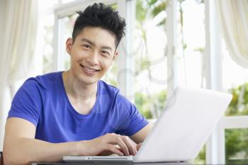 Young Chinese Man Sitting At Desk Using Laptop At Home