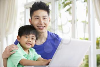Chinese Father And Son Sitting At Desk Using Laptop At Home