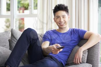Young Chinese Man Sitting And Watching TV On Sofa At Home