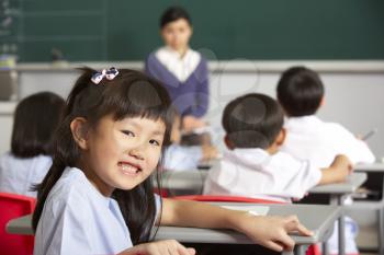 Portrait Of Female Pupil Working At Desk In Chinese School Classroom