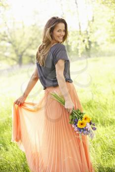 Woman Walking Through Summer Field Carrying Bouquet Of Flowers