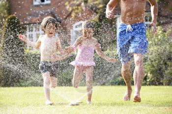 Father And Two Children Running Through Garden Sprinkler
