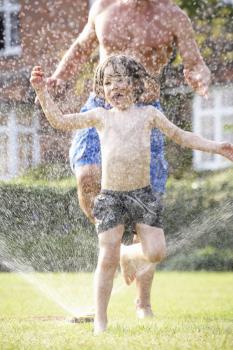 Father And Son Running Through Garden Sprinkler