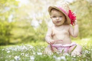Baby Girl In Summer Dress Sitting In Field Wearing Sunglasses And Straw Hat