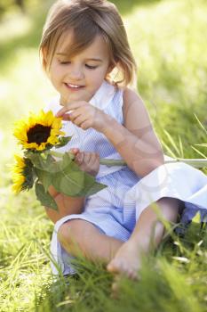 Young Girl Sitting In Summer Field Holding Sunflower