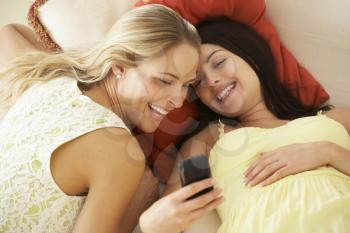 Two female Friends On Sofa Reading Text Message