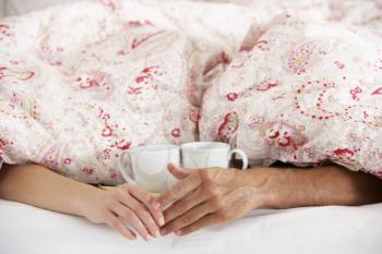 Romantic Couple Holding Hands Under Duvet In Bed