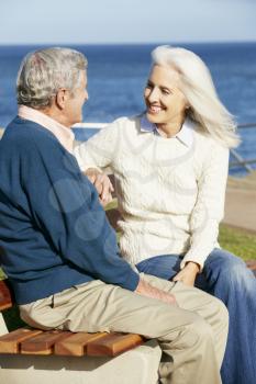 Senior Couple Sitting On Bench By Sea Together
