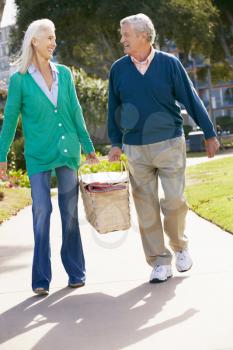 Senior Couple Walking In Park Together With Picnic Basket