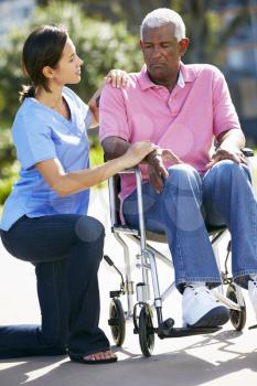 Carer Pushing Unhappy Senior Man In Wheelchair