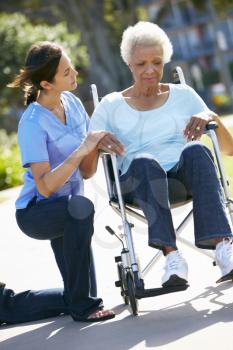 Carer Pushing Unhappy Senior Woman In Wheelchair