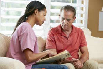 Nurse Discussing Records With Senior Male Patient During Home Visit