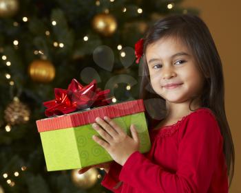 Girl Holding Christmas Present In Front Of Tree