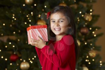 Girl Holding Christmas Present In Front Of Tree