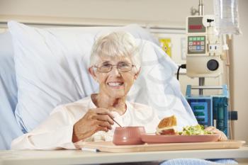 Senior Female Patient Eating Meal In Hospital Bed