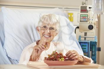 Senior Female Patient Eating Grapes In Hospital Bed