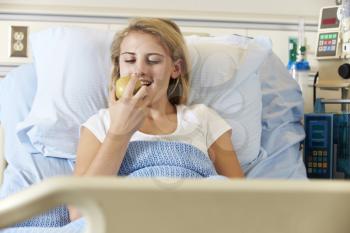 Teenage Female Patient Eating Apple In Hospital Bed