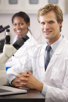 Male And Female Scientists Using Microscopes In Laboratory