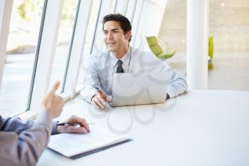 Two Businessmen Having Meeting Around Table In Modern Office