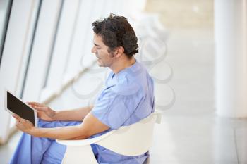 Male Nurse Sitting In Chair Using Digital Tablet