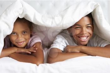Two Children Hiding Under Duvet In Bed