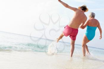 Senior Couple Splashing In Sea On Beach Holiday