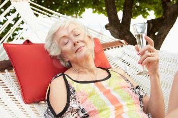 Senior Woman Relaxing In Beach Hammock With Champagne