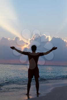 Silhouette Of Man With Outstretched Arms On Beach At Sunset