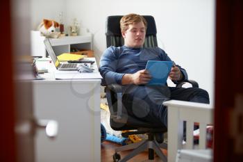 Teenage Boy Using Digital Tablet In Bedroom