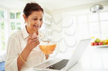 Senior Indian Woman Using Laptop Whilst Eating Breakfast