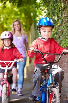 Children Riding Bikes On Their Way To School With Mother