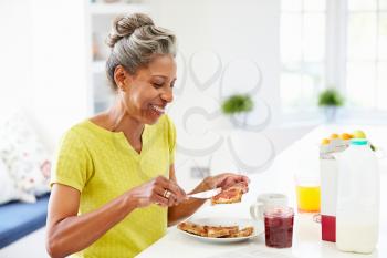 Mature Woman Eating Breakfast Spreading Jam On Toast