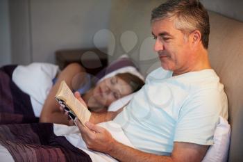 Middle Aged Couple In Bed Together With Man Reading Book